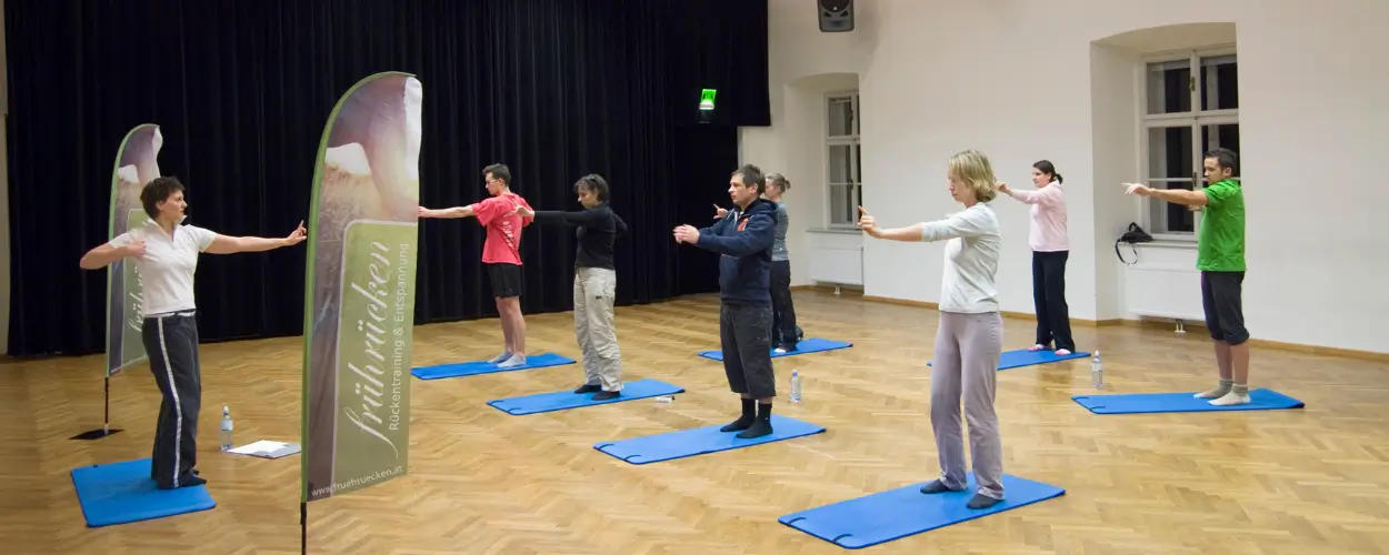 Gruppe beim Rückentraining auf blauen Matten im Museumsquartier Wien mit frührücken-Banner